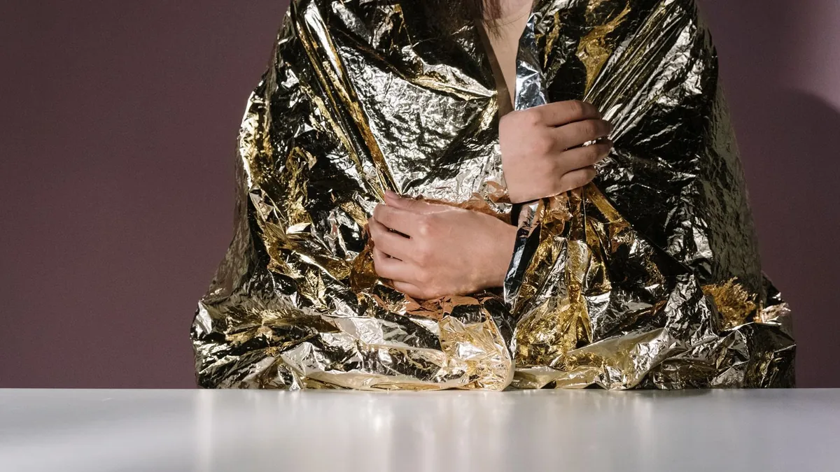 A person wrapped in an orange reflective emergency blanket on a cold morning beside a vehicle