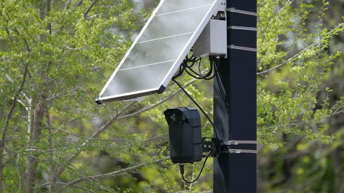A small LoRa radio board in a weatherproof box mounted on a pole with a solar panel against the sky