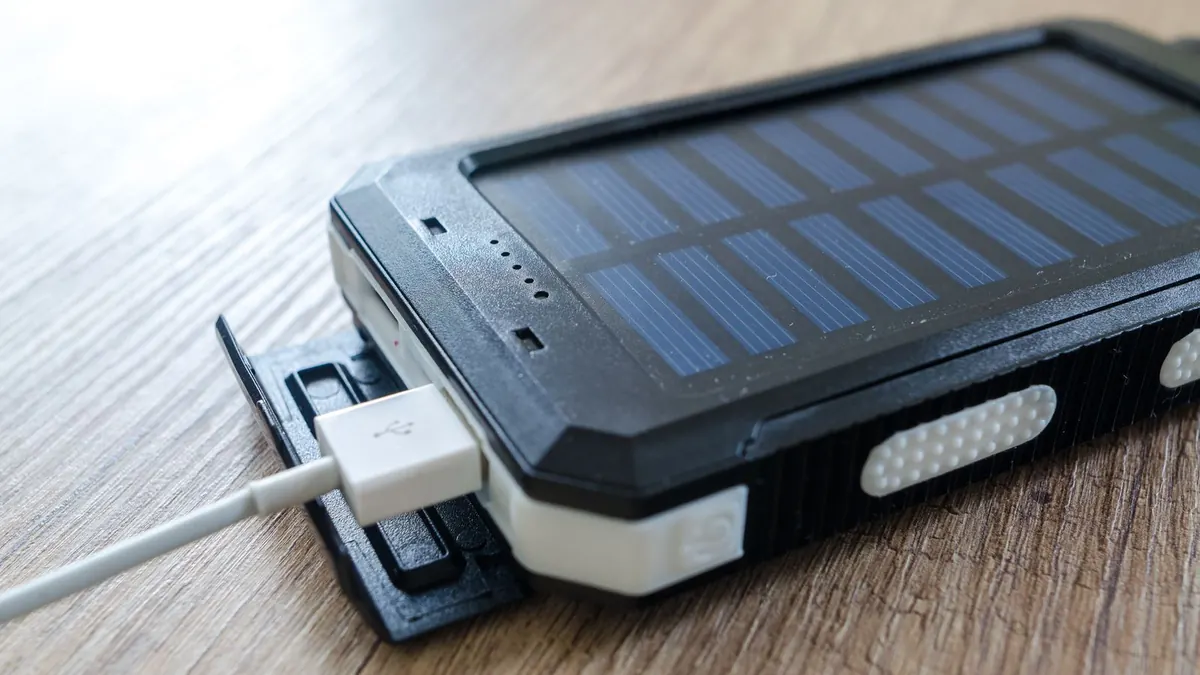 A folding solar panel on a porch rail charging a phone power bank