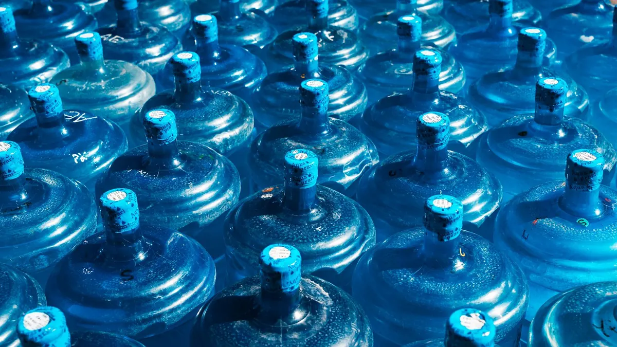 Blue stackable water storage tanks and jugs lined up in a basement closet