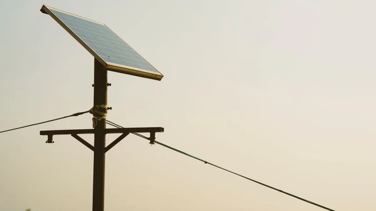 A small solar panel and weatherproof box with an antenna mounted on a pole against a clear sky